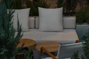 A well-lit living area with two couches, chairs, and potted plants, featuring white pillows and a clean, elegant atmosphere