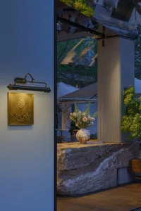 A warm and inviting cafe space with a stone countertop, potted plants, and a vase of flowers, set up for outdoor seating with multiple umbrellas