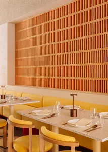 Modern restaurant interior with wooden panel walls, tables, chairs, and couches, featuring wine glasses and a stylish atmosphere