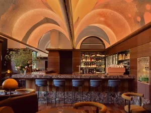 A cozy bar area with a long wooden counter featuring a marble top, surrounded by chairs and bottles of alcoholic beverages