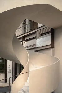 A modern building with a spiral staircase leading to another level, featuring large windows that allow natural light to enter the space, creating an atmosphere of elegance and sophistication
