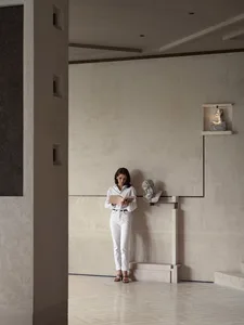 A woman reads a book in a calm, empty room with a white color scheme