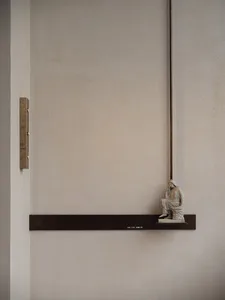 A calm and serene interior space with a concrete wall, a small statue on a ledge, and two lights, creating a peaceful atmosphere