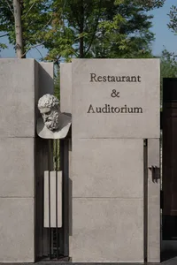 A stone wall with a marble bust of a man, a sign reading Restaurant & Auditorium, and a sophisticated interior space