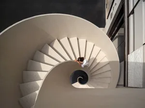 A spiral staircase in a well-lit building with concrete steps, suggesting a sense of depth and intrigue