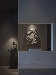 A modern art gallery featuring a stone sculpture on a wall, surrounded by a neutral background, with a warm and inviting atmosphere