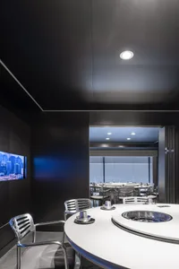 A modern restaurant dining area with multiple tables and chairs, surrounded by windows allowing natural light to enter the space