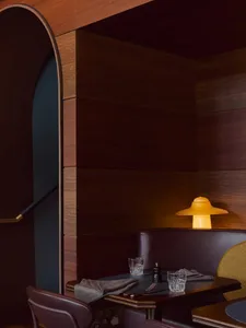 Warm and inviting restaurant interior with wooden walls and floors, featuring two dining tables with chairs, cups, and a vase, creating a cozy atmosphere