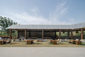 Outdoor dining space with tables, chairs, and umbrellas under a large roof structure