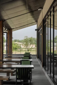 A warm and inviting dining area with multiple wooden tables and green cushioned chairs, perfect for social gatherings or meals