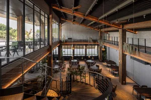 Spacious dining area with multiple tables and chairs, high ceilings, and large windows allowing natural light to fill the room