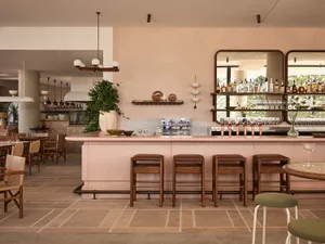 A cozy bar area with a pink marble counter, wooden stools, and various bottles and tableware