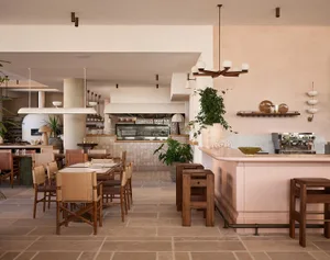 A modern restaurant with a pink bar, wooden furniture, and stone elements, featuring warm white and brown tones and overhead lighting