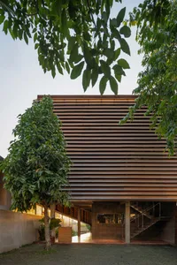 A large wooden building with a unique design, surrounded by two trees and a peaceful atmosphere