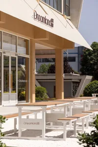 Architectural rendering of a modern building with a wooden facade, metal roof, and multiple windows, surrounded by outdoor benches
