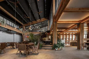 Open living area with wooden floors and walls, featuring multiple chairs, dining tables, and a potted plant, creating a warm and inviting atmosphere