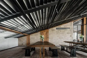 Cozy dining area with a long wooden table and benches, surrounded by chairs, in a dimly lit rustic space