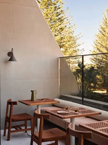 A modern living area with a combination of wood and concrete elements, featuring a dining table, chairs, couches, and potted plants, creating a welcoming and functional space