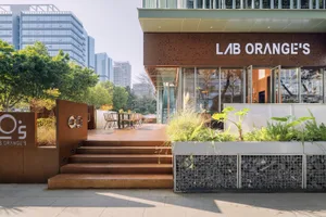 A modern building's exterior features a large patio area with multiple chairs and dining tables, creating a welcoming atmosphere for guests to enjoy meals