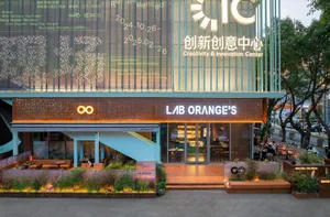 充滿活力的橙色牆面零售空間，擁有大型櫥窗展示、多樣陳列物品，周圍環繞著人群