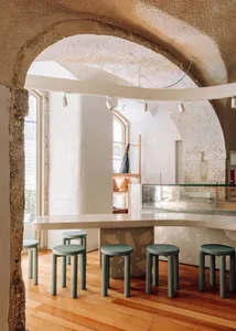 A cozy cafe interior with a wooden counter, glass display case, and five stools, creating an inviting atmosphere for socializing and dining
