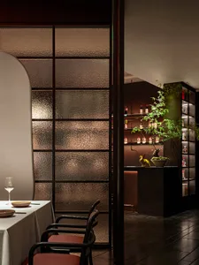 Sophisticated restaurant interior with a dining table, chairs, and a kitchen in the background, featuring wooden accents and wine bottles