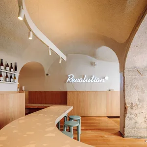 Modern restaurant bar with a counter and chairs, featuring bottles and a mix of natural and artificial lighting