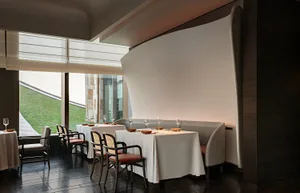 Elegant dining space with a large wooden table and chairs, set with wine glasses and bowls, in a sophisticated restaurant atmosphere