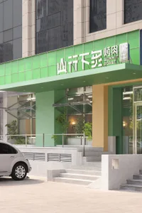 Asian restaurant with green walls, a green roof, and a welcoming atmosphere, featuring a sign in English and Chinese, potted plants, and a parked car