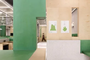 A calm and orderly hallway with a green wall, wooden panels, and a white floor, featuring two people walking down the hallway