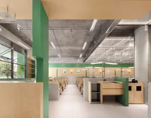 Open office space with a large green wall, wooden floors and walls, and multiple tables and chairs with potted plants