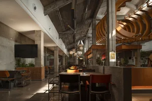 A modern restaurant interior with a large dining area featuring multiple tables and chairs, well-lit for a comfortable atmosphere