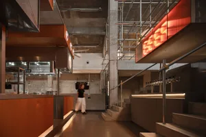 A modern restaurant and bar area with a woman walking down a hallway between two staircases, surrounded by bottles and stylish decor