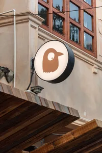 Modern building exterior with a lit bird logo on the facade, white walls, and two clocks on the wall