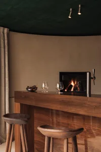 Cozy living space with a wooden bar counter, wine glasses, and a chair, featuring warm and inviting atmosphere
