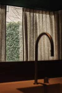 Bathroom with a metal sink under a window, surrounded by curtains, with natural light entering through the window