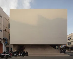 A modern building with a blank white wall, surrounded by motorcycles and people standing around the area