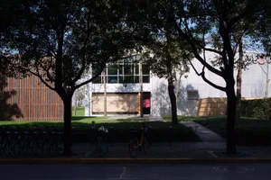 Modern building with a large window, surrounded by trees and bicycles, in a urban setting