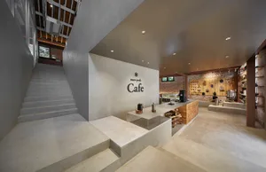 A modern cafe interior with a concrete wall, a counter, and various cups and bottles on display