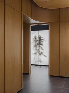 A well-lit interior hallway with wooden walls and floors, featuring a painting of trees on one door and a bright atmosphere