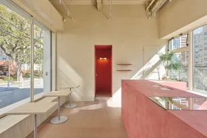 Warm and inviting restaurant interior with a red doorway, two dining tables, chairs, and bottles on the right side