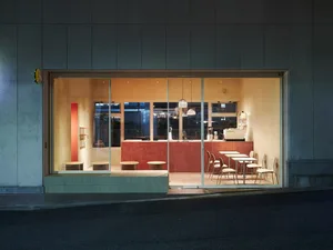 A modern restaurant interior at night with wood flooring, white walls, and comfortable seating arrangements around dining tables