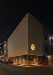 A calm night scene of a large white building with a yellow sign and two people standing outside