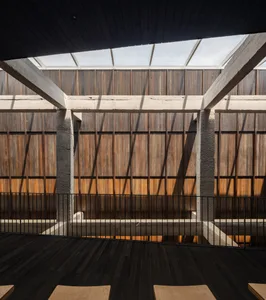 A large building with wooden walls and floors, featuring multiple rooms and hallways, with a warm and rustic atmosphere, and chairs placed within the space
