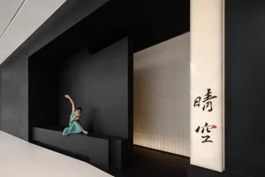 An Asian woman poses in front of a black wall in a contemporary interior with a bench and artistic composition