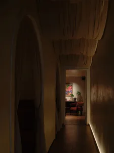 A dimly lit hallway with a yellow wall, two chairs, and a potted plant, creating a cozy atmosphere