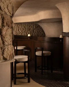 Cozy bar area with a stone wall, wooden floors, and a brown bar counter, lit by two lamps