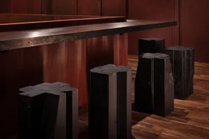 A wooden bar counter in a restaurant setting with four black stools and a warm atmosphere