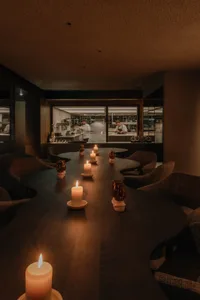 Warm and inviting restaurant interior with a large dining table, wooden chairs, and candles, set against a background kitchen