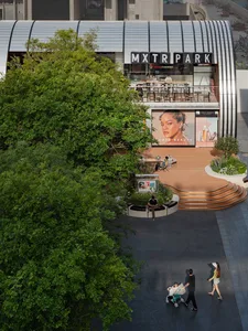 Lively outdoor shopping area with modern architecture, glass structure, and natural light, featuring people walking and engaging in activities